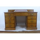 An early 20th century oak twin pedestal desk with writing slope to top with tooled red leather