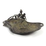 An Art Nouveau metalware ovoid dish in the form of a lounging well dressed lady reading,