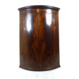 A Georgian flame mahogany and shell inlaid bow fronted corner cupboard,