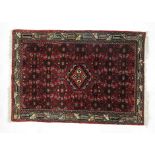 A hand woven Persian rug thee triple lined border enclosing a red ground field with a central