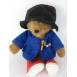 A stuffed Paddington Bear with orange button eyes, wearing a blue coat, black hat,