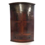 An 18th century mahogany bow fronted wall hanging corner cupboard with two doors over single drawer