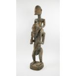 TRIBAL ARTS, Dogon figural carving of a man being carried on the shoulders of an ancestors, 85cm H.