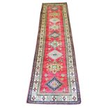 KAZAK RUNNER, 295cm x 82cm, row of stylised medallions on a ruby field within complimentary borders.