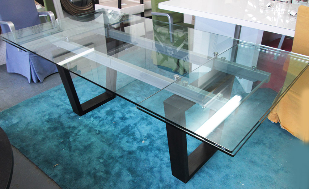 DINING TABLE, with glass top and pull out leaves to end on a metal and ebonised base,