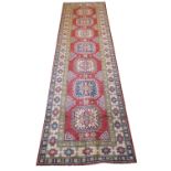 KAZAK RUNNER, 322cm x 83cm, of multiple medallions on ruby field within ivory borders.