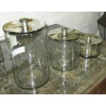 COOKIE JARS, graduated set of three, in glass with chromed metal lids, largest 35cm H.