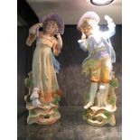 A pair of Bisque figures depicting a boy and a girl with dogs at their feet, 31cm high