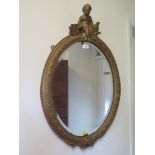 A Victorian giltwood oval mirror, surmounted by a cherub, 79cm high