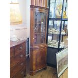 A crossbanded walnut corner cabinet, with glazed door over a bowed cupboard door on bracket feet,