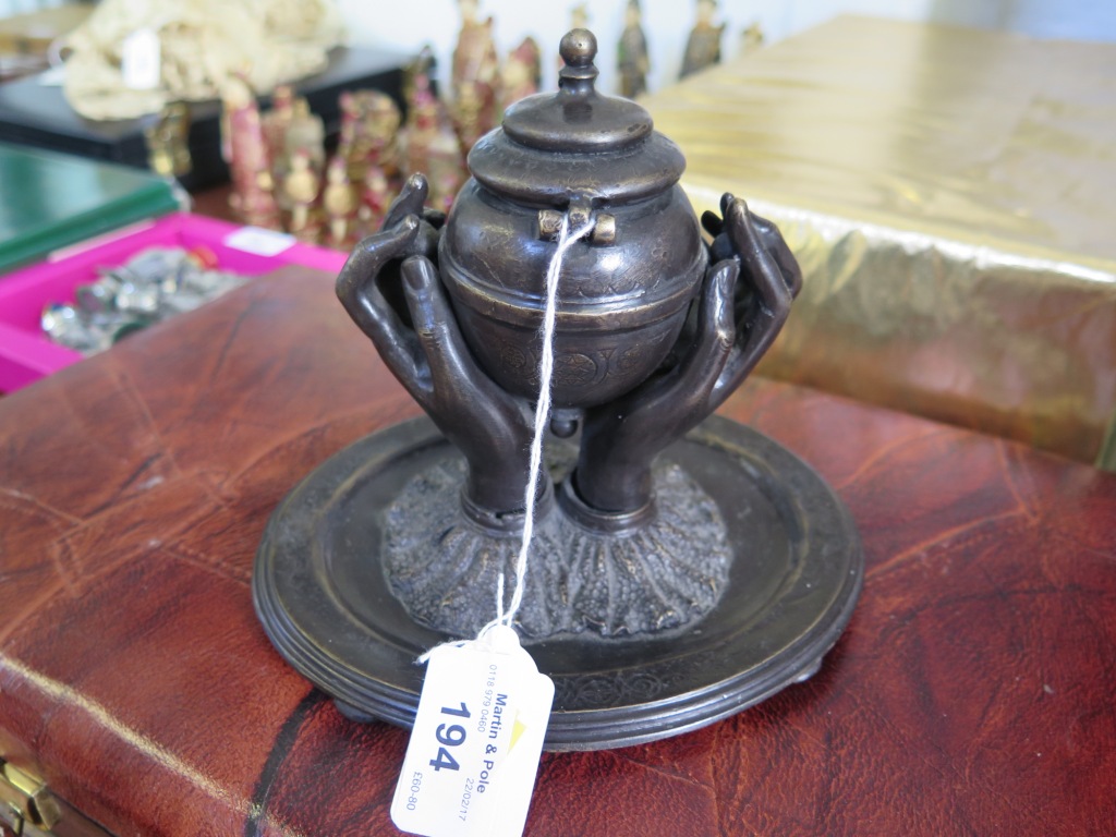 A 19th century bronze inkwell in the form of two hands holding an urn, on an oval base. 16.5cms wide