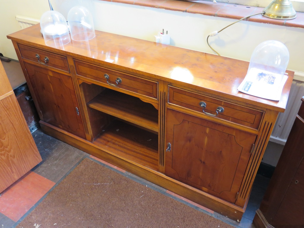 A yewwood veneer crossbanded sideboard with three drawers over open shelves flanked by cupboard