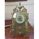 An early 20th century gilt brass easel timepiece, the arched scrolling pierced frame with urn,