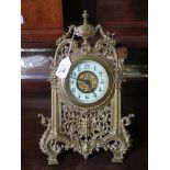 An early 20th century gilt brass easel timepiece, the arched scrolling pierced frame with urn,