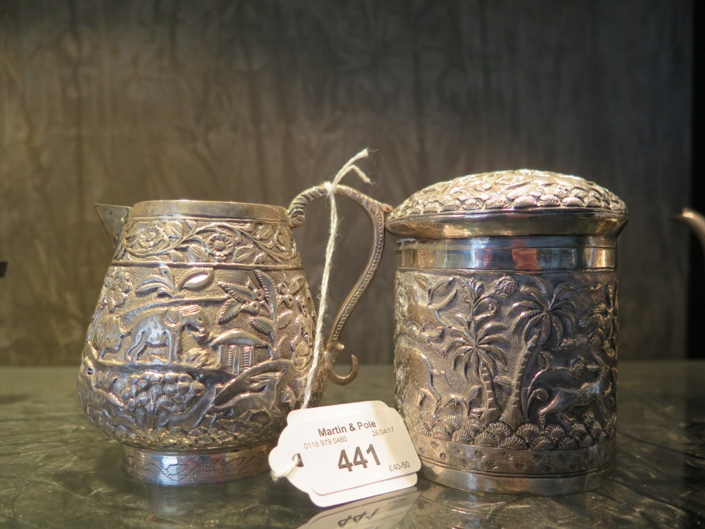 A silver colour metal Indian cream jug decorated in relief with flora and fauna and a box with lid