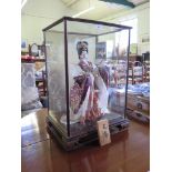 A Japanese Geisha girl doll, holding a fan, in an inscribed bevelled glass case 61cm high