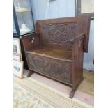 A carved oak monk's bench, the hinged top/back carved with dragons over a lidded seat carved with