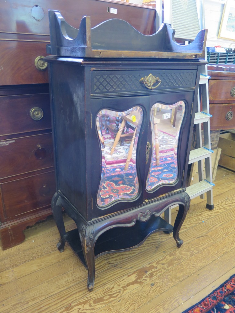 An Edwardian ebonised and mirrored music cabinet, the raised swan neck back over a drawer and pair