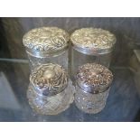 Four glass and silver lidded vanity jars, the lids decorated in high relief