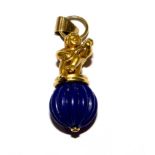 An 18 carat gold pendent of a putti sitting on a lapiz lazuli ball