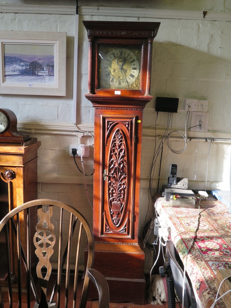 An oak longcase clock, the carved frieze over a brass dial with gilt mask spandrels, subsidiary