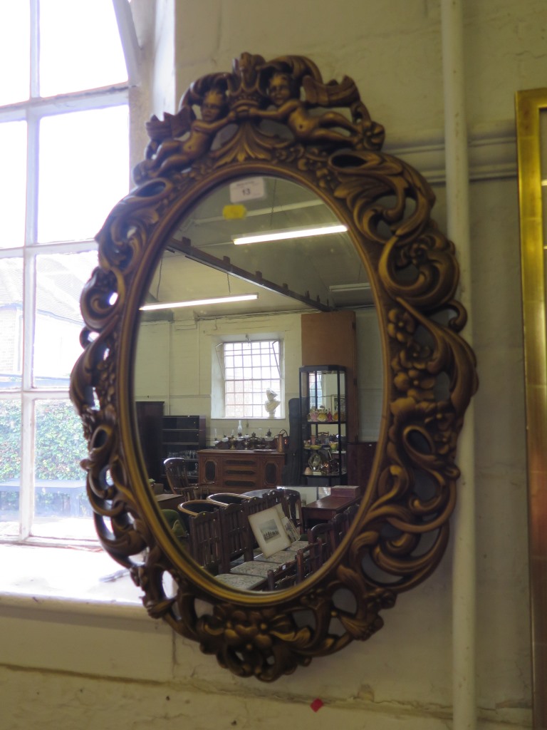An oval gilt framed wall mirror with putti crest, 67cm high