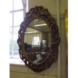 An oval gilt framed wall mirror with putti crest, 67cm high