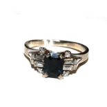 A white gold metal ring, set with a trap cut sapphire with baguette and round diamonds to each side