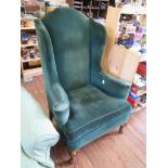 A George II style green upholstered wing armchair, on cabriole legs and pad feet