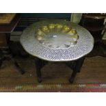 An Indian brass circular table top with dished centre, on carved wood folding trestle base 78cm