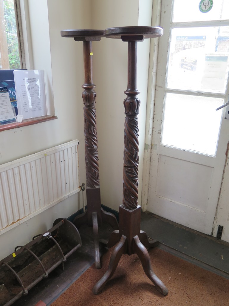 A pair of mahogany torchere stands, formerly bedposts, with foliate carving and quadruped bases,