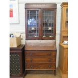 A 1920s oak bureau bookcase with lead glazed doors, falling slope and three long graduated drawers