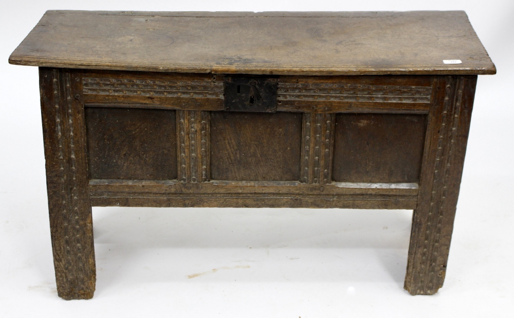 A 17TH CENTURY OAK COFFER with plank top, panelled front, chip carved decoration and standing on