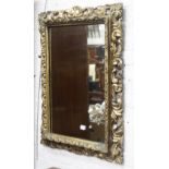 AN ANTIQUE GILT CARVED GESSO PICTURE FRAME with mirror plate within, 85cm x 86cm overall