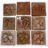 A GROUP OF NINE TERRACOTTA TILES with leaf decoration, mushrooms and fruit (9)