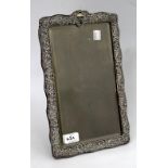AN ANTIQUE SILVER FRAMED EASEL BACKED MIRROR with scrolling foliate decoration, makers marks
