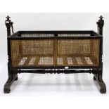 AN ANTIQUE TURNED HARDWOOD CHILD'S CRADLE with caned sides and stand with scrolling feet, 119cm wide