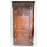 A GEORGE III OAK STANDING CORNER CABINET with shaped fielded panel doors, standing on a plinth base,