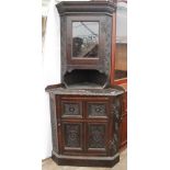 A CARVED OAK CORNER CABINET with a glazed door above a panelled door and raised on a plinth base,