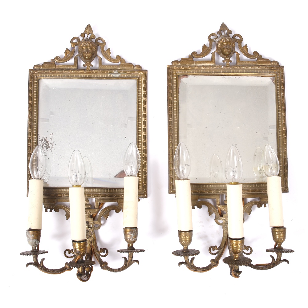 A PAIR OF CAST BRASS THREE BRANCH GIRANDOLE WALL LIGHTS with mask decoration, bevelled mirror