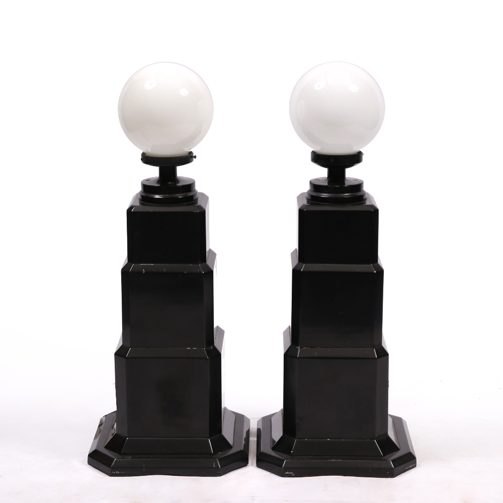 A PAIR OF ART DECO EBONISED LAMP STANDS with white glass spheres on the stepped bases, each 34cm