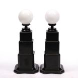 A PAIR OF ART DECO EBONISED LAMP STANDS with white glass spheres on the stepped bases, each 34cm