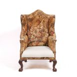 A GEORGIAN TAPESTRY UPHOLSTERED WING ARMCHAIR with camel back standing on ball and claw feet,