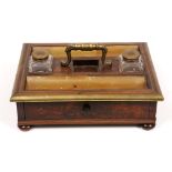 AN ANTIQUE ROSEWOOD AND BRASS BOUND DESK STAND with loop handle, glass inkwells, brass lined pen