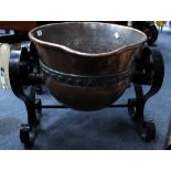 AN ANTIQUE RIVETED COPPER VESSEL on a scrolling wrought iron stand, reputedly used in the