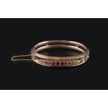 A GEM SET BANGLE, of hinged bifurcated form, centred with a navette-shaped panel of circular-cut red