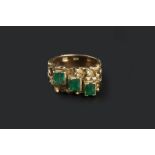 AN EMERALD DRESS RING, of abstract textured design, highlighted with a trio of rectangular step-