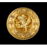 AN ARCHAEOLOGICAL REVIVAL GOLD PANEL BROOCH, the circular concave panel depicting cupid seated on