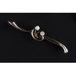 A DIAMOND SET BAR BROOCH, the stylised scrolled bar highlighted with two obliquely set round