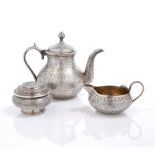 AN INDIAN WHITE METAL TEAPOT and matching milk jug with cobra handle and all over chased foliate